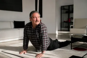 Sabah oturma odasındaki halının üzerinde yavaş esneme hareketleri yapan orta yaşlı bir adam