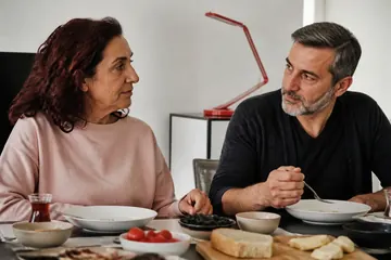 Sabah ışığında evde sakin ve acelesiz bir kahvaltı paylaşan yaşlı bir kadın ve yetişkin oğlu