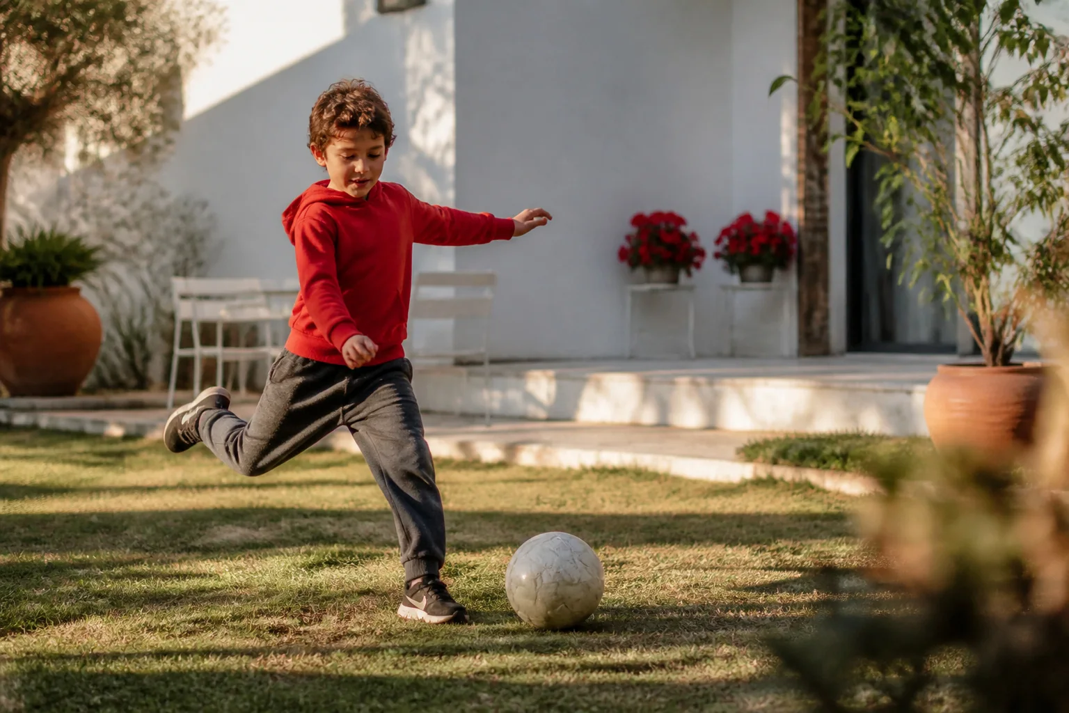 Altın renkli akşam ışığında bahçede futbol topuna vuran bir erkek çocuk