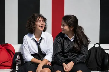 Okul çıkışı bir park bankında, sırt çantaları yanlarında, birlikte kahkaha atan on beş yaşında iki kız arkadaş