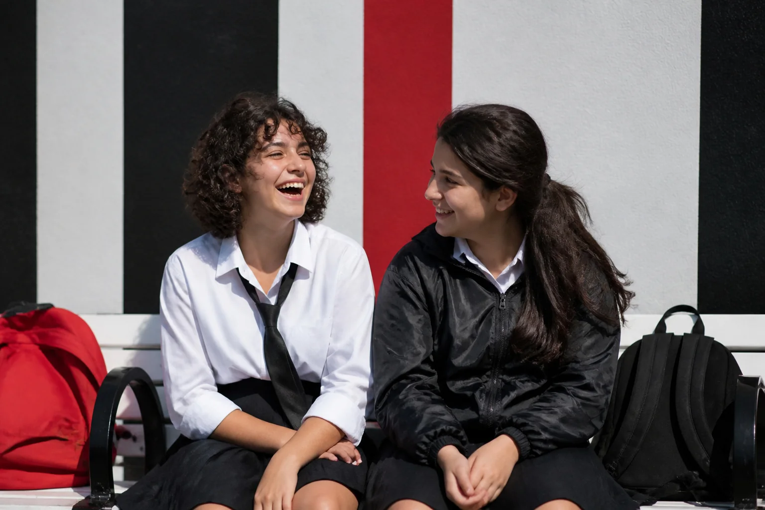 Okul çıkışı bir park bankında, sırt çantaları yanlarında, birlikte kahkaha atan on beş yaşında iki kız arkadaş